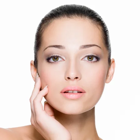 A young woman touches her smooth, hairless face and stares at the camera