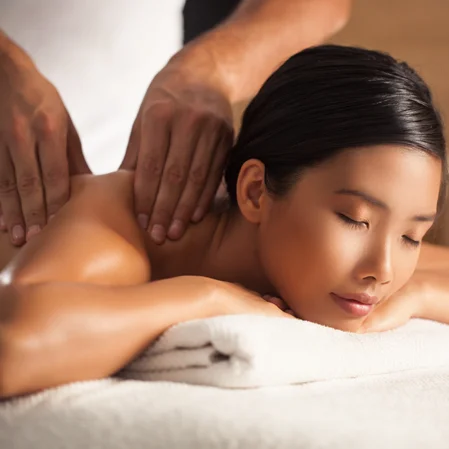 A young woman lays on a massage table in relaxation while a massage therapist massages her shoulder